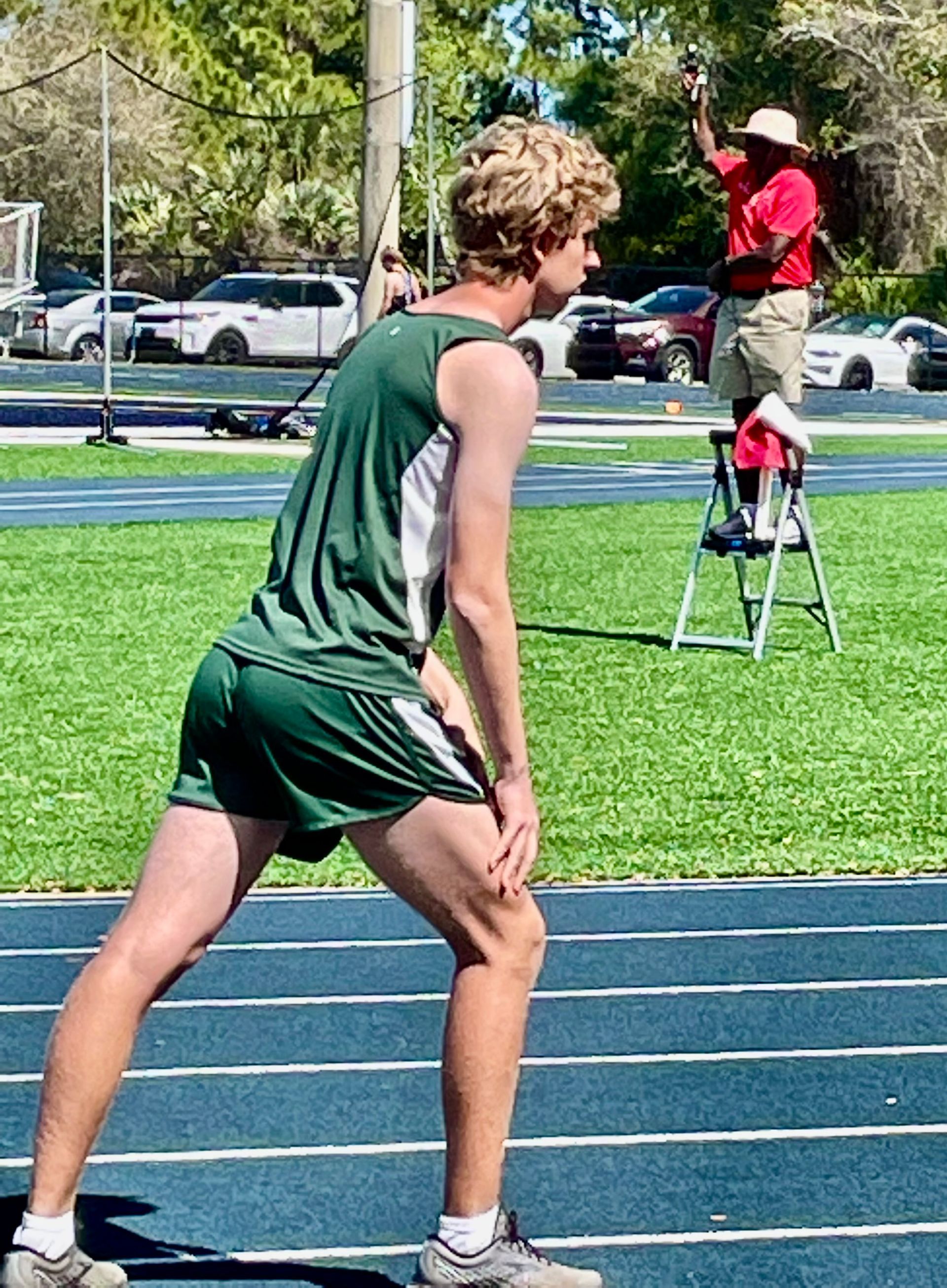 A young man is stretching on a track while a man stands on a ladder.