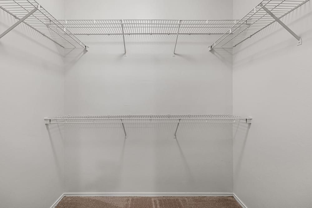 Empty walk-in closet with white walls and multiple wire shelves on the upper sides, and beige carpet flooring at Marquis at Stonebriar in Frisco, TX.