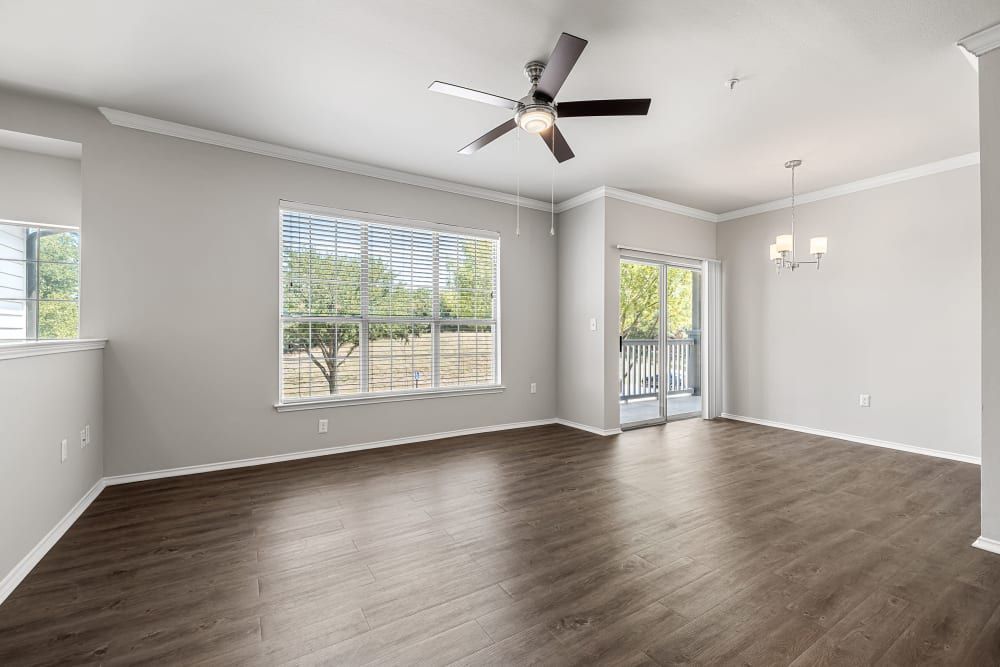 Spacious and empty room interior with large windows, blinds, a ceiling fan, and sliding glass door leading to a balcony at Marquis at Stonebriar in Frisco, TX.