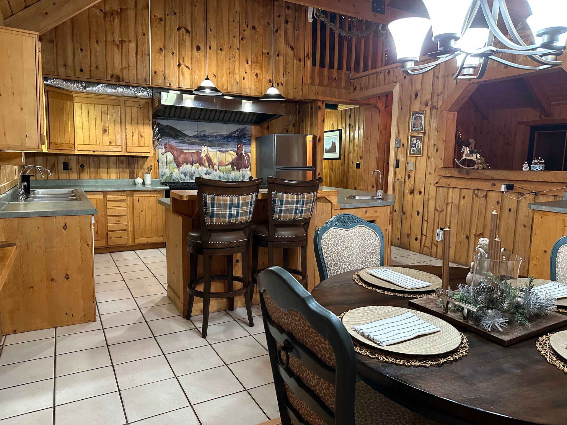 Rustic wood kitchen with a stainless steel refrigerator, light countertops, and hanging mugs beneath a small window.
