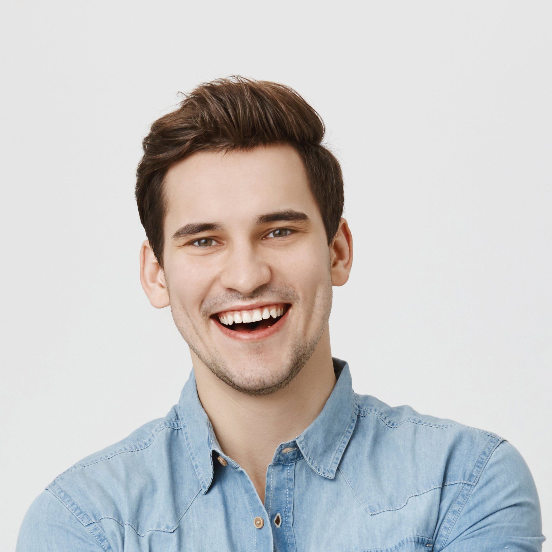 A young man in a denim shirt is smiling and looking at the camera.