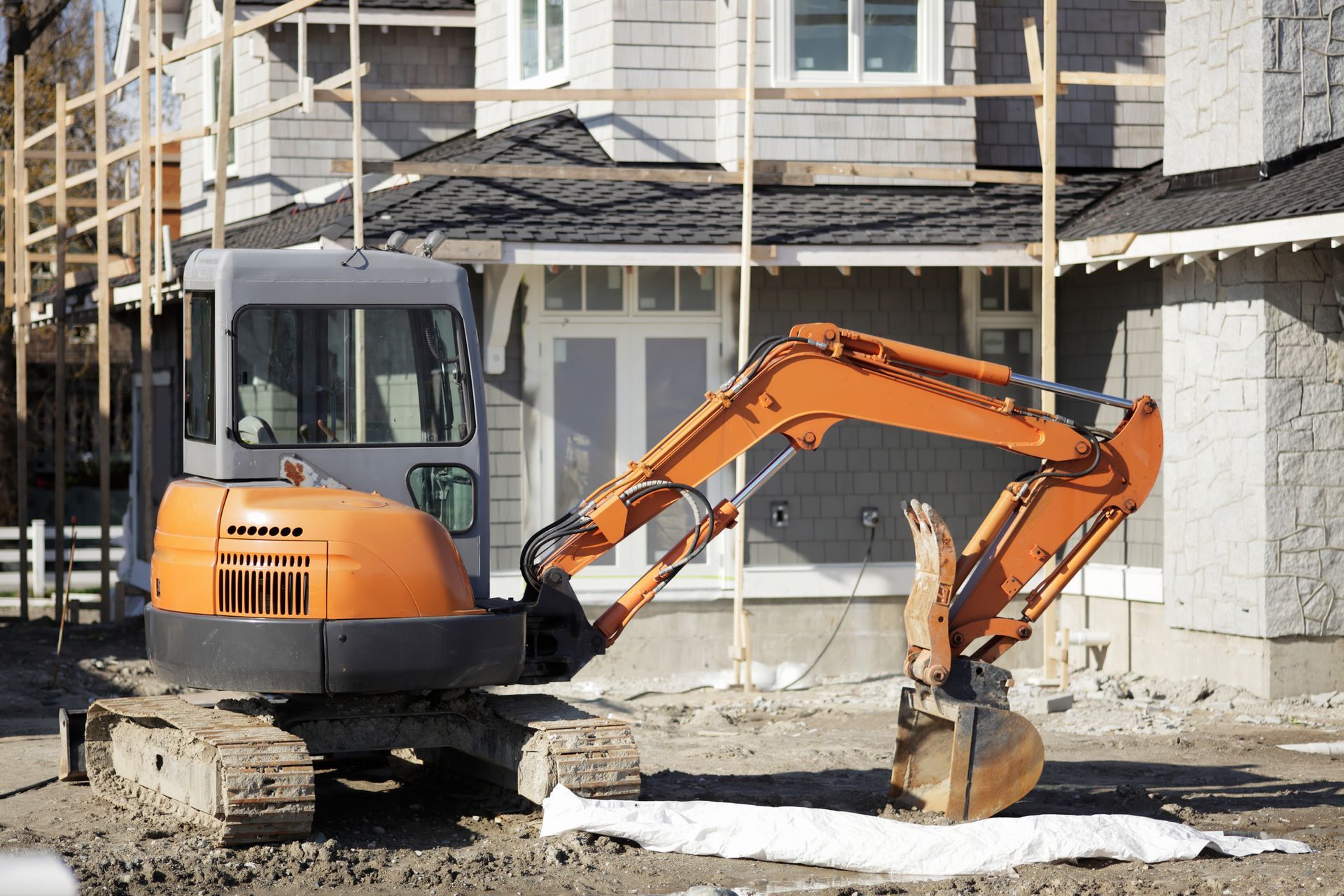 An orange excavator is parked in front of a house under construction.