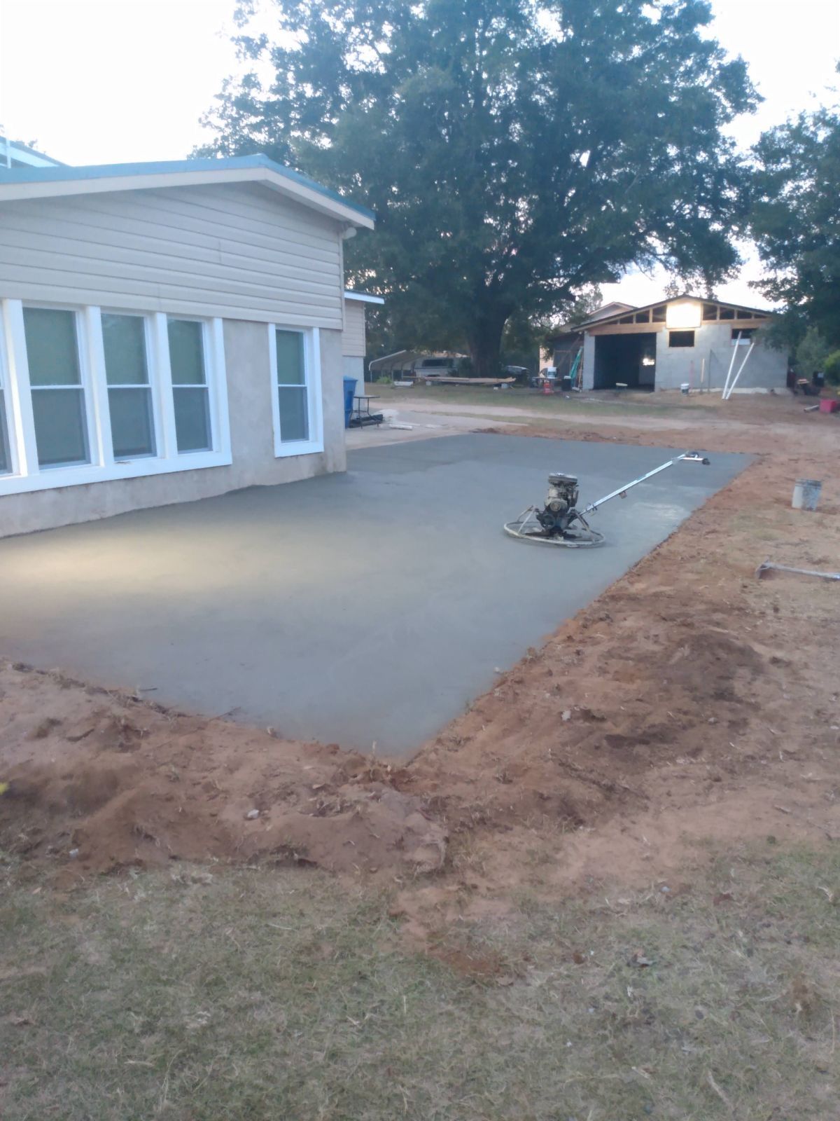 Freshly poured concrete patio next to a house with windows, construction in the background.