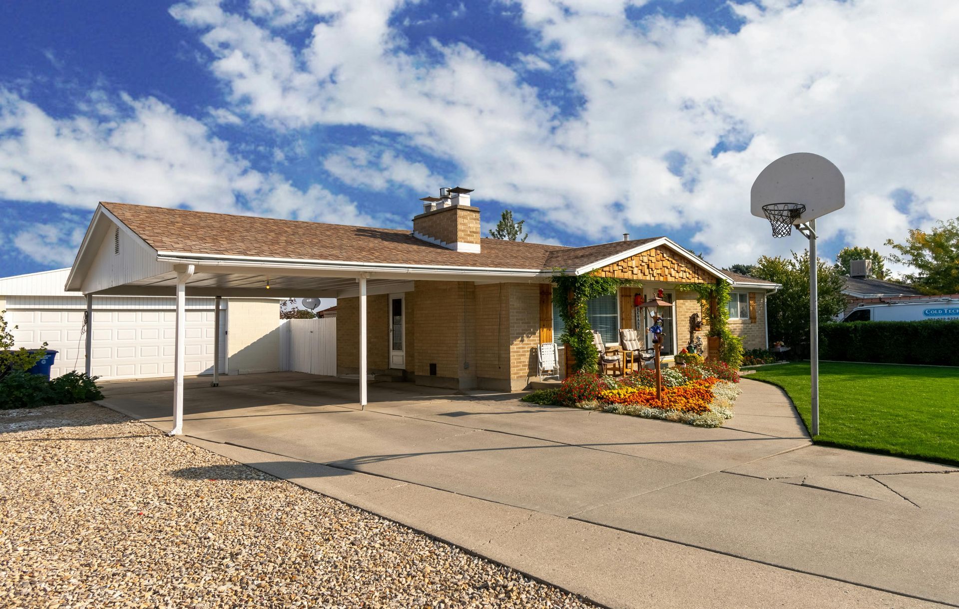 House with carport, driveway, and basketball hoop on a sunny day.