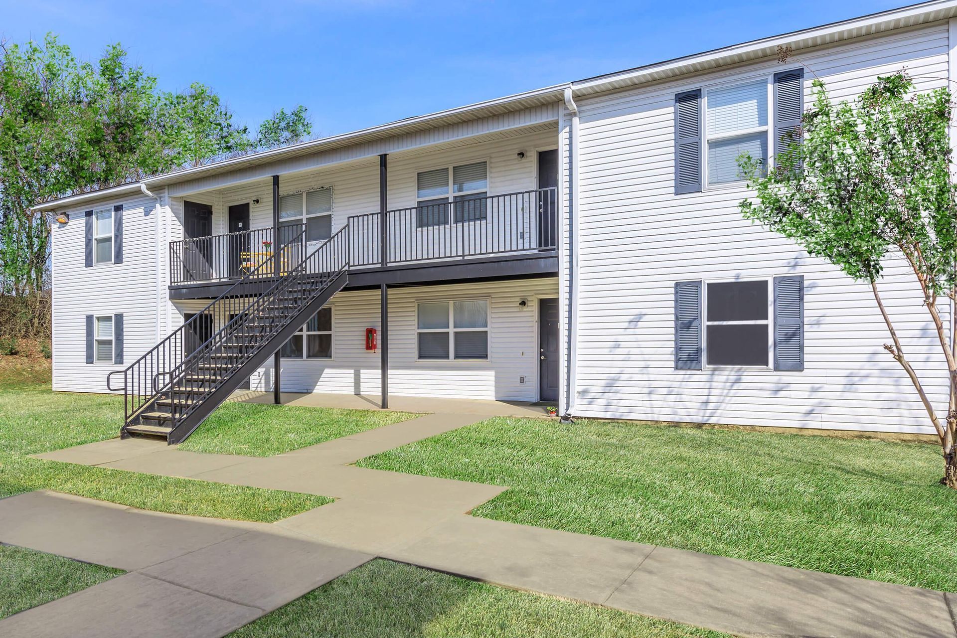 Two-story white apartment building with black staircases and a green lawn.