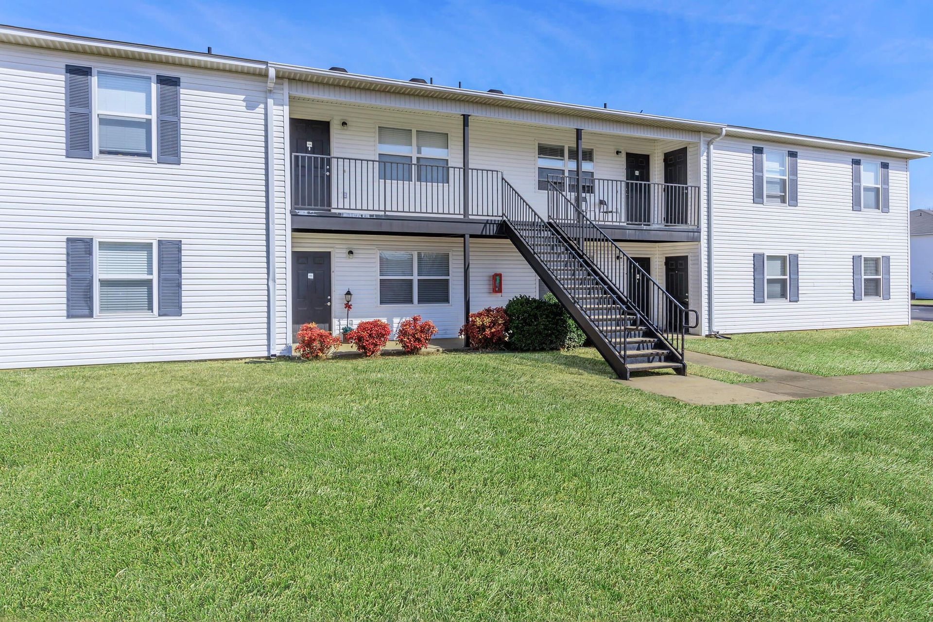 Two-story white apartment building with black stairwell and shutters; green lawn.