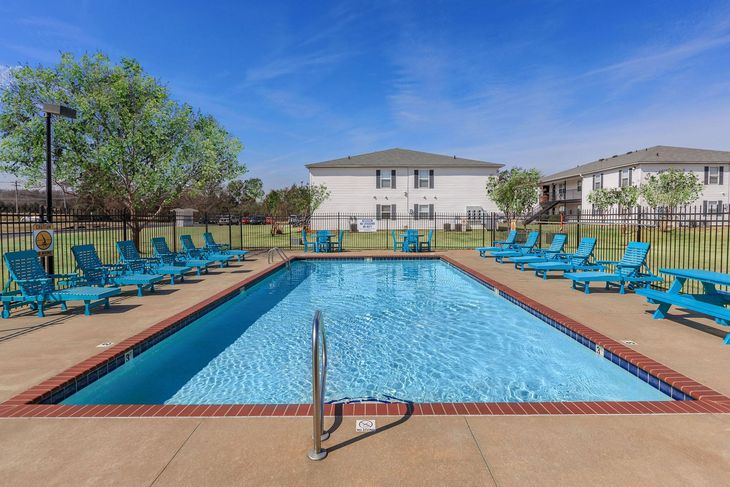 Swimming pool with blue lounge chairs and apartment buildings on a sunny day.