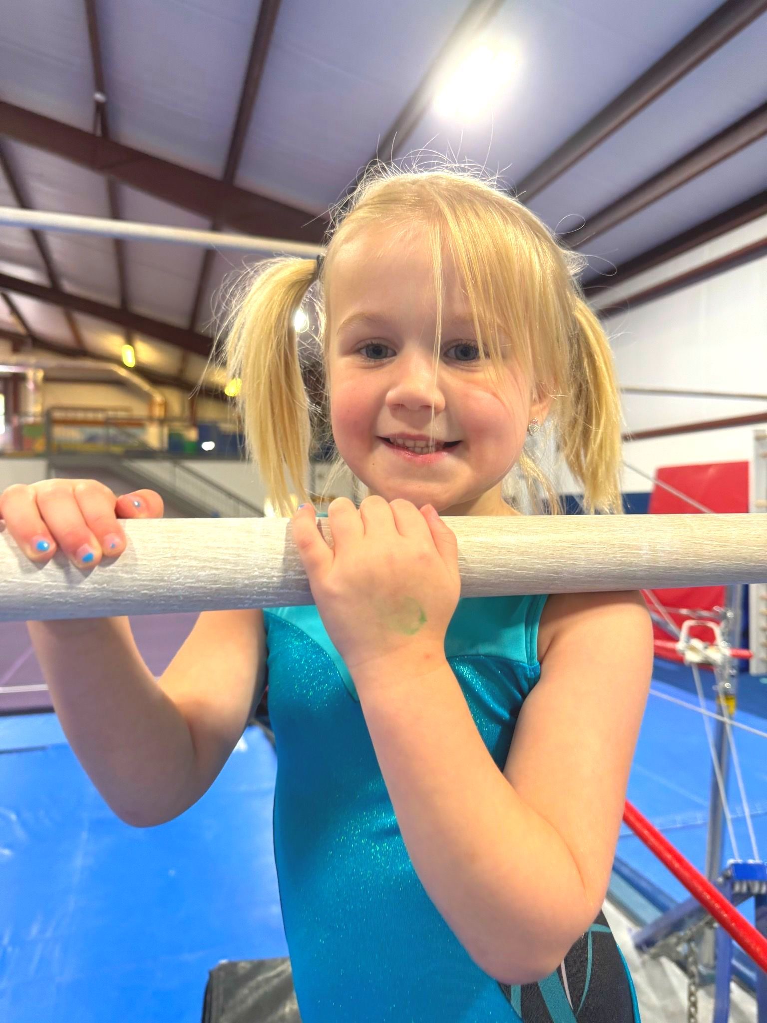 A little girl is hanging on a bar in a gym.