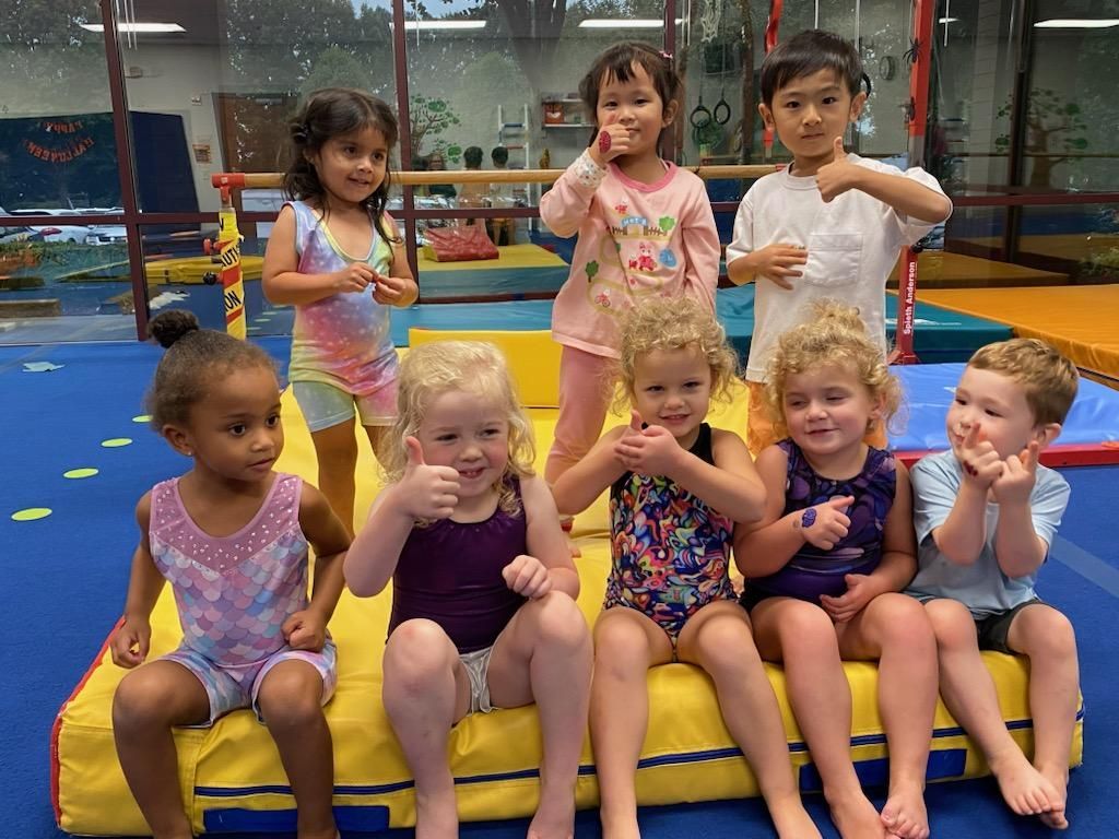 A group of young children are sitting on a mat in a gym.