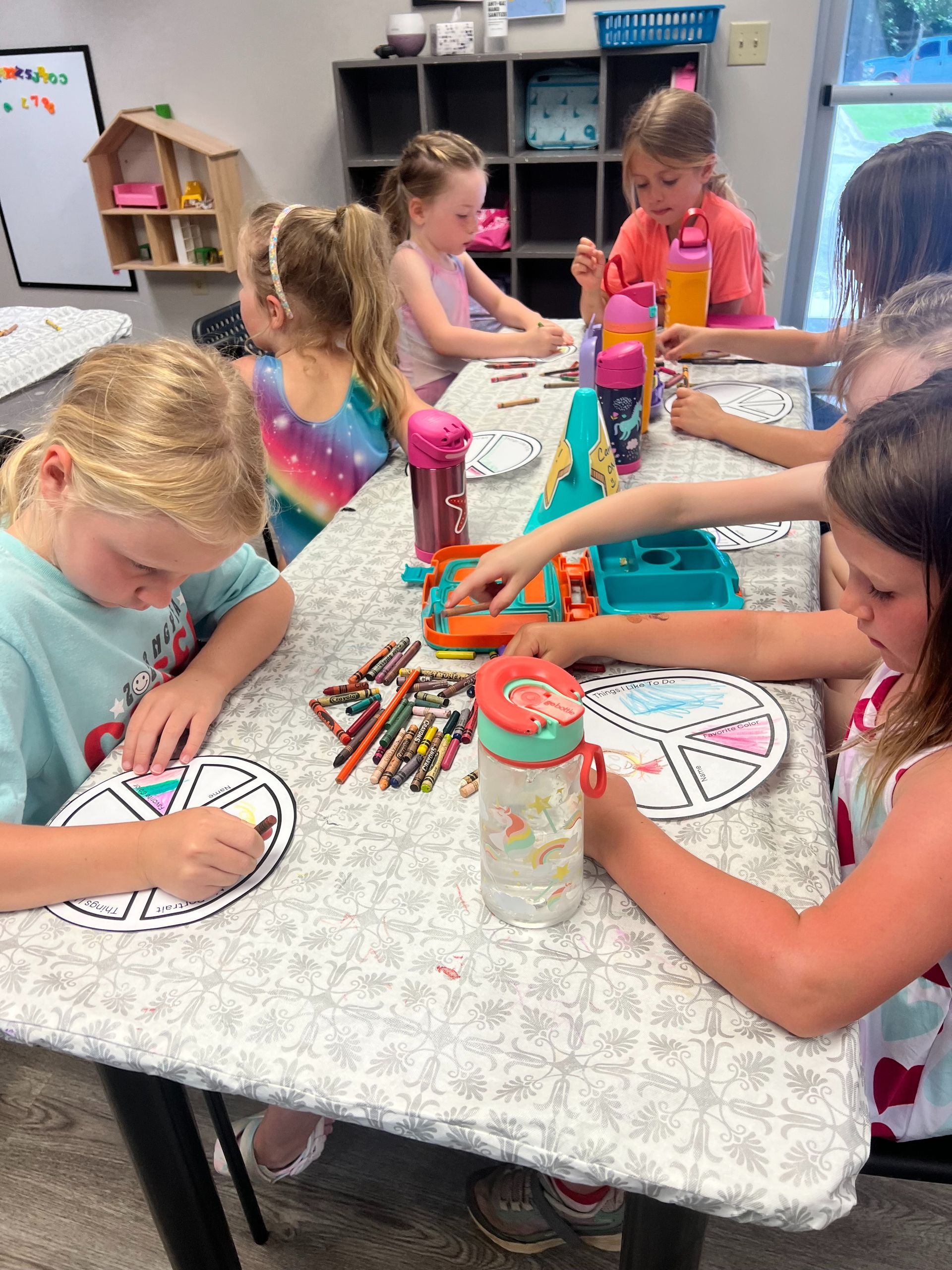 A group of young girls are sitting at a table drawing on paper.