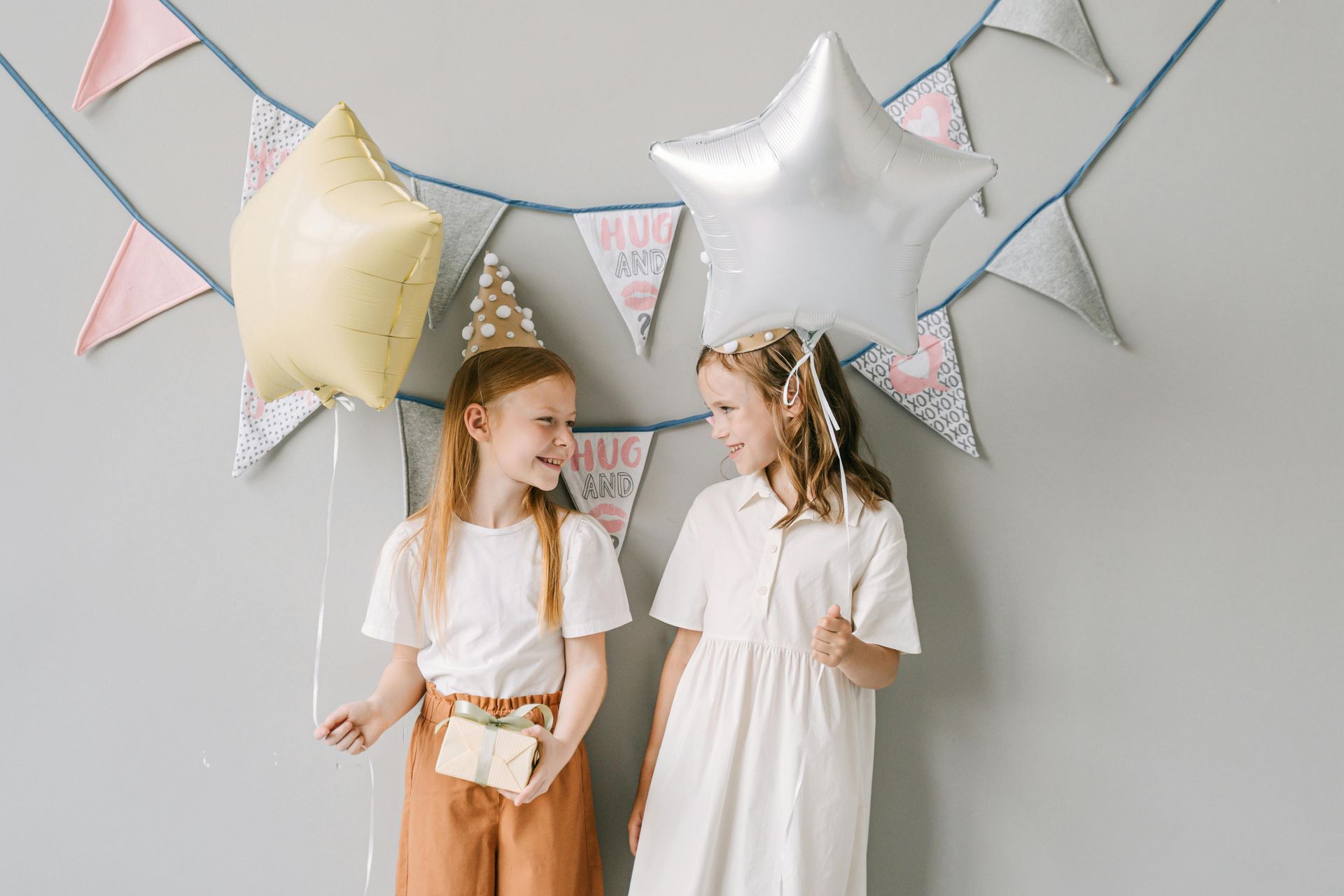 Two little girls are standing next to each other with balloons and flags.