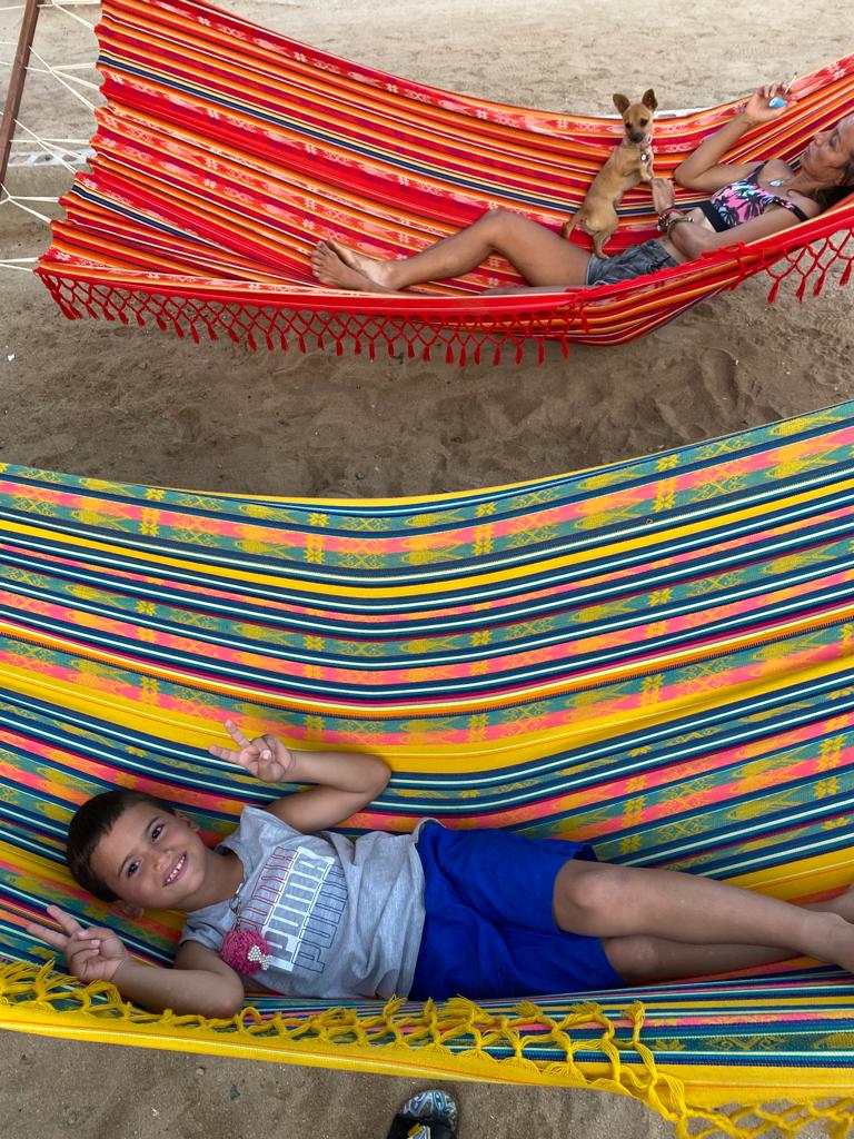 A boy and a girl are laying in hammocks on the beach.
