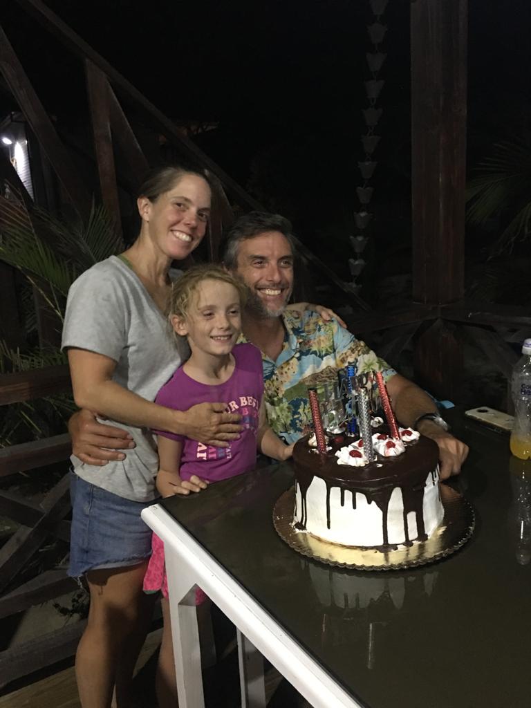 A man and woman are standing next to a little girl in front of a birthday cake.