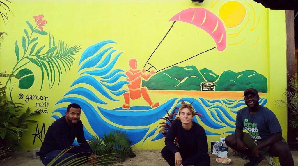 Three people are posing in front of a mural of a man parasailing