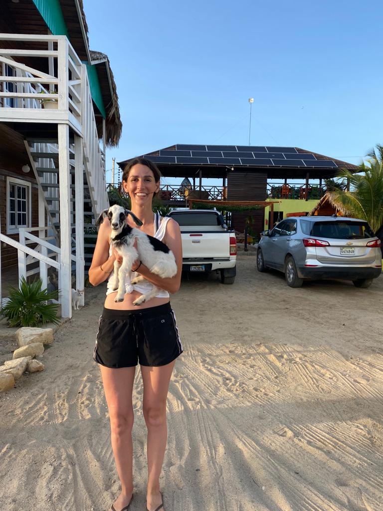 A woman is holding a small dog in front of a building.