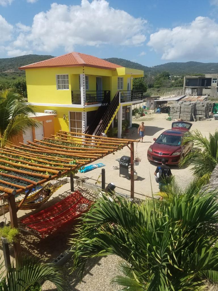 A yellow house with a red roof and a red car parked in front of it.