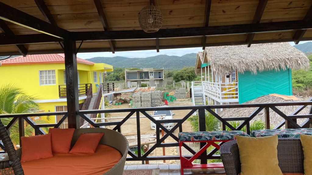 A balcony with a couch and chairs and a view of a yellow house.