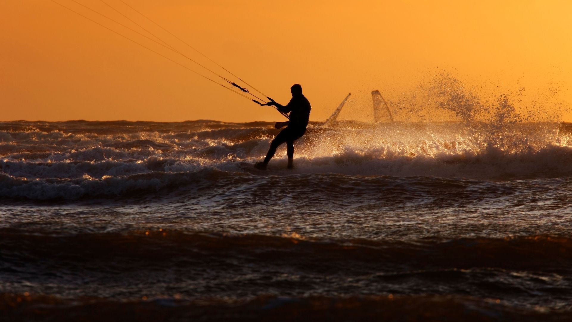 A man is flying a kite in the ocean at sunset.