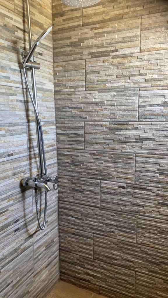 A shower with a tiled wall and a shower head.