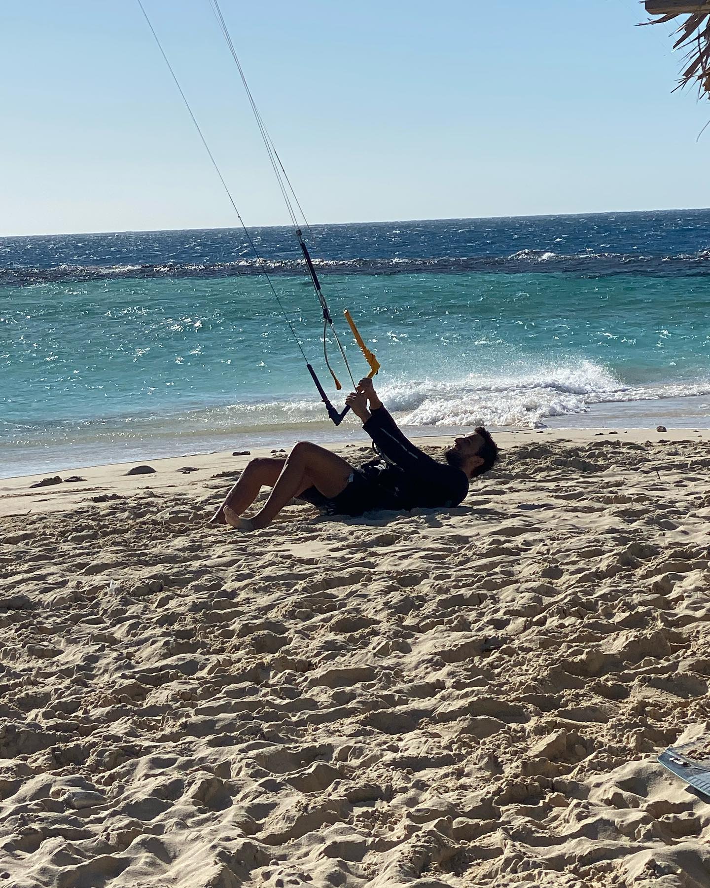 A person is laying on the beach holding a kite.