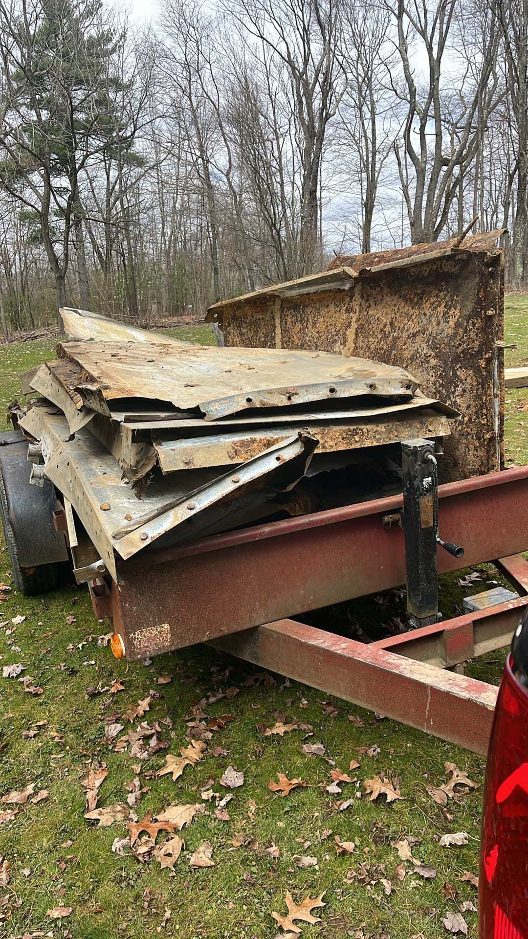 A trailer with a pile of wood on it is parked in the grass next to a truck.