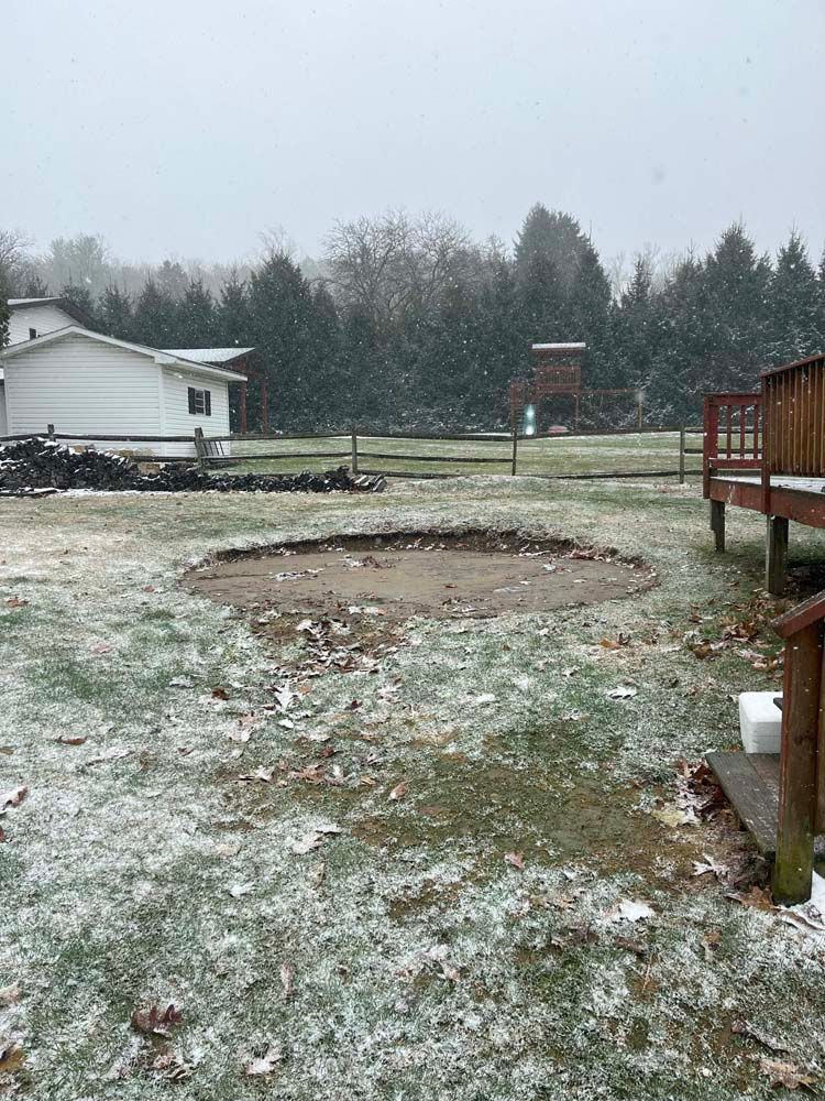 A snowy yard with a house in the background and a fence in the foreground.