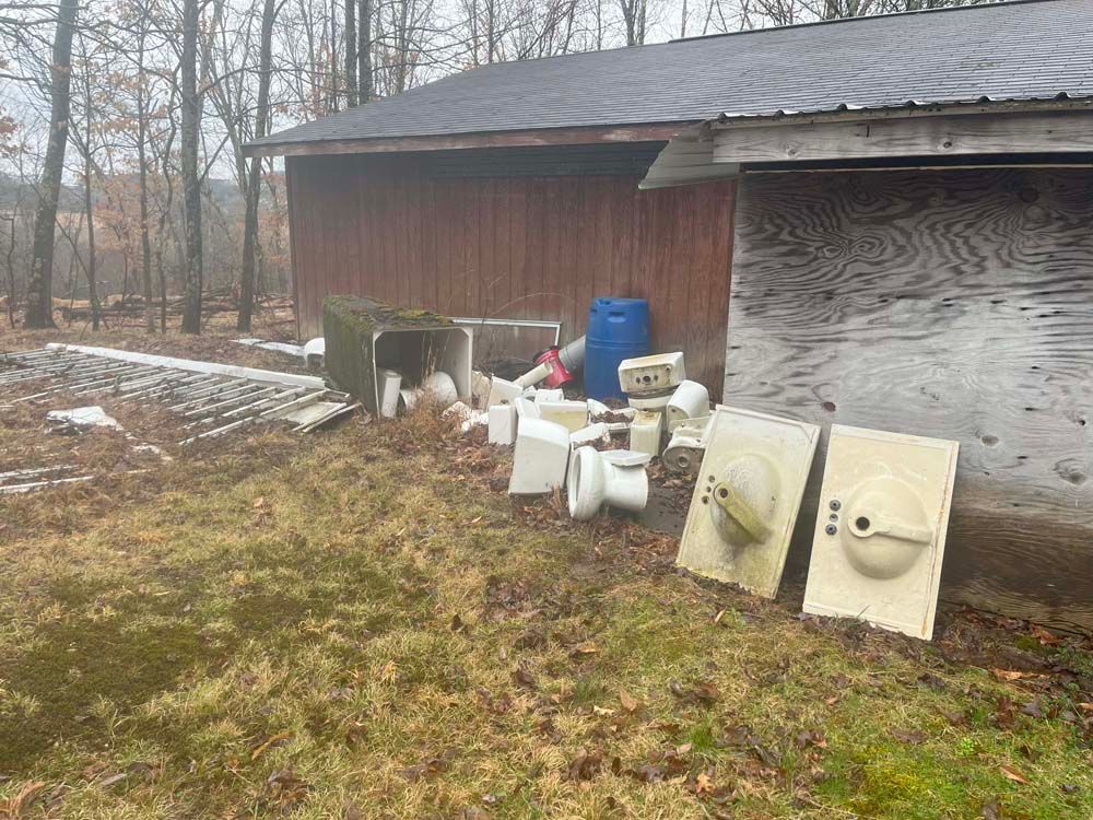 A pile of trash is sitting in the grass in front of a wooden building.