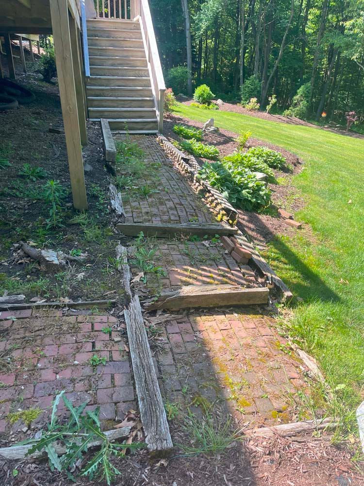 A brick walkway with stairs leading up to a deck in a backyard.