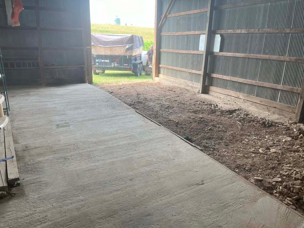 A concrete walkway leading to a barn with a truck parked in the background.