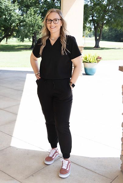 A woman wearing glasses and a black shirt is leaning against a wall in a hallway.