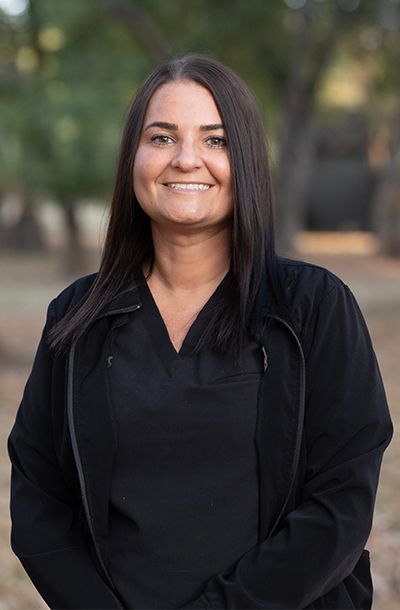 A woman in a black jacket is leaning against a wall and smiling.