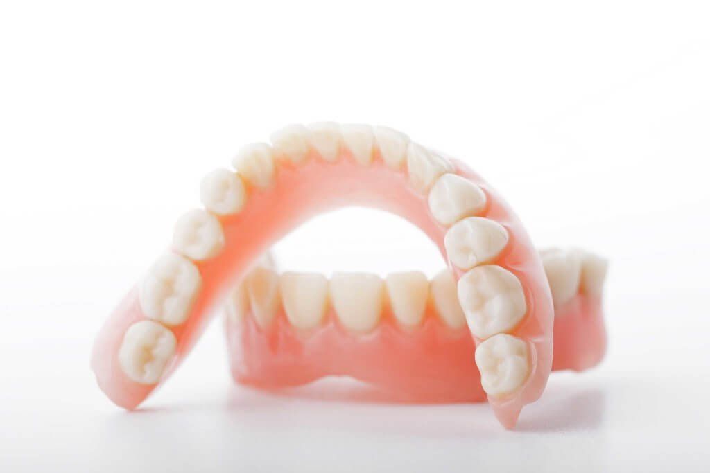 A pair of dentures sitting on top of each other on a white surface.