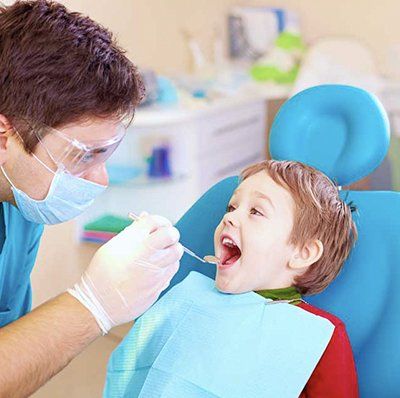 A dentist is examining a young boy 's teeth in a dental chair.