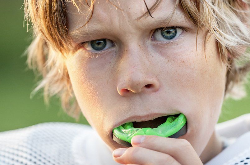 A young boy is wearing a green mouth guard.