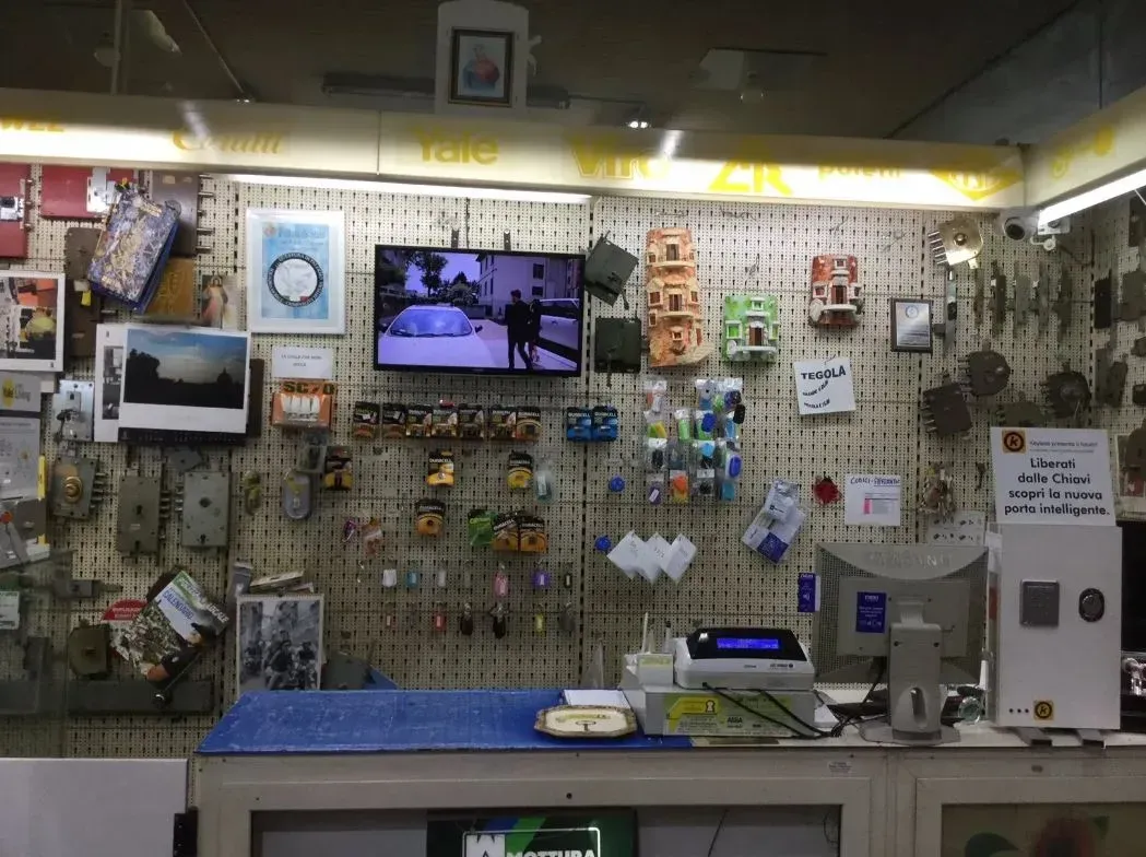 Un bancone di ferramenta disordinato con vari articoli in vendita e un piccolo televisore acceso.