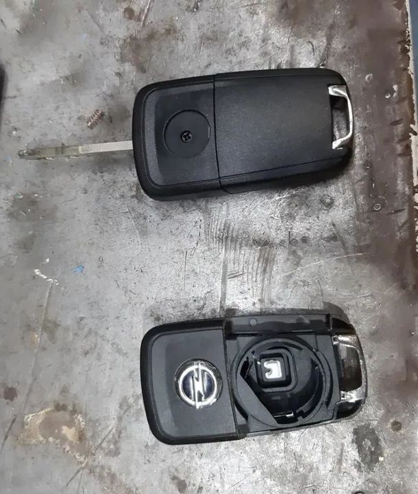 Due chiavi nere per auto, una intatta e l'altra aperta, che rivelano i componenti interni, appoggiate su una superficie metallica.