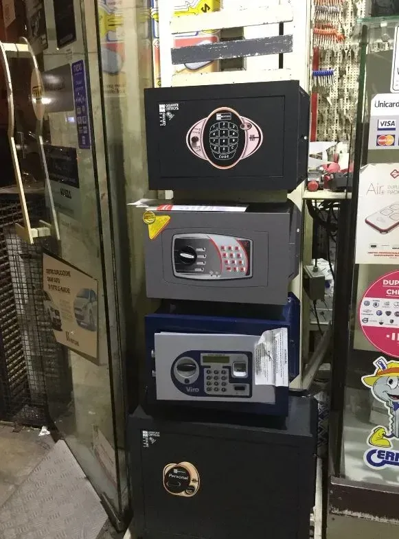 Quattro casseforti di vari colori impilate nella vetrina di un negozio. Sono visibili le tastiere digitali.