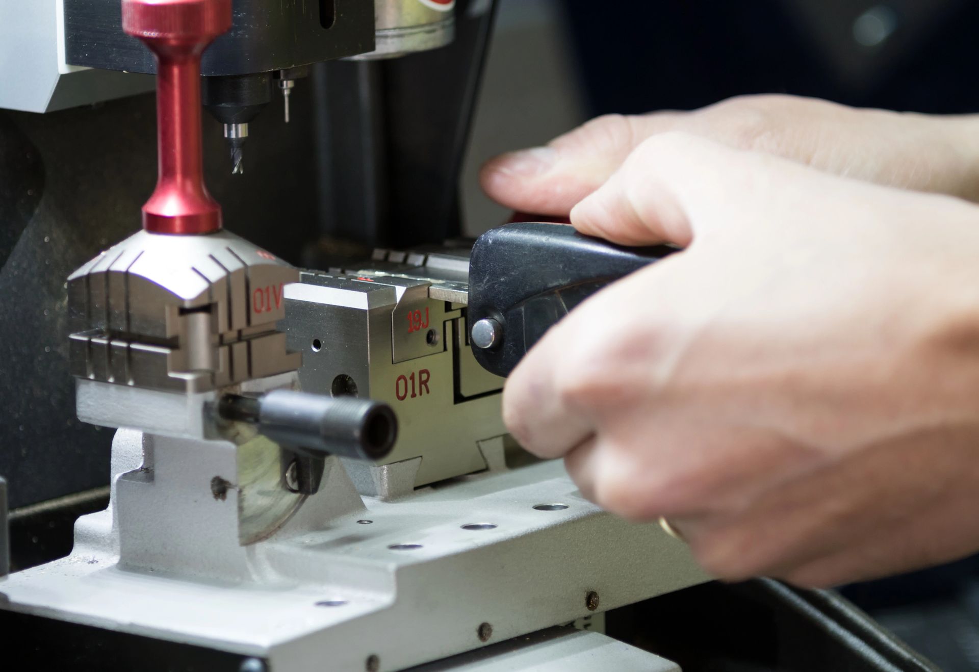 Le mani azionano una macchina duplicatrice di chiavi, preparandosi a duplicare una chiave con un meccanismo di taglio color argento e rosso.