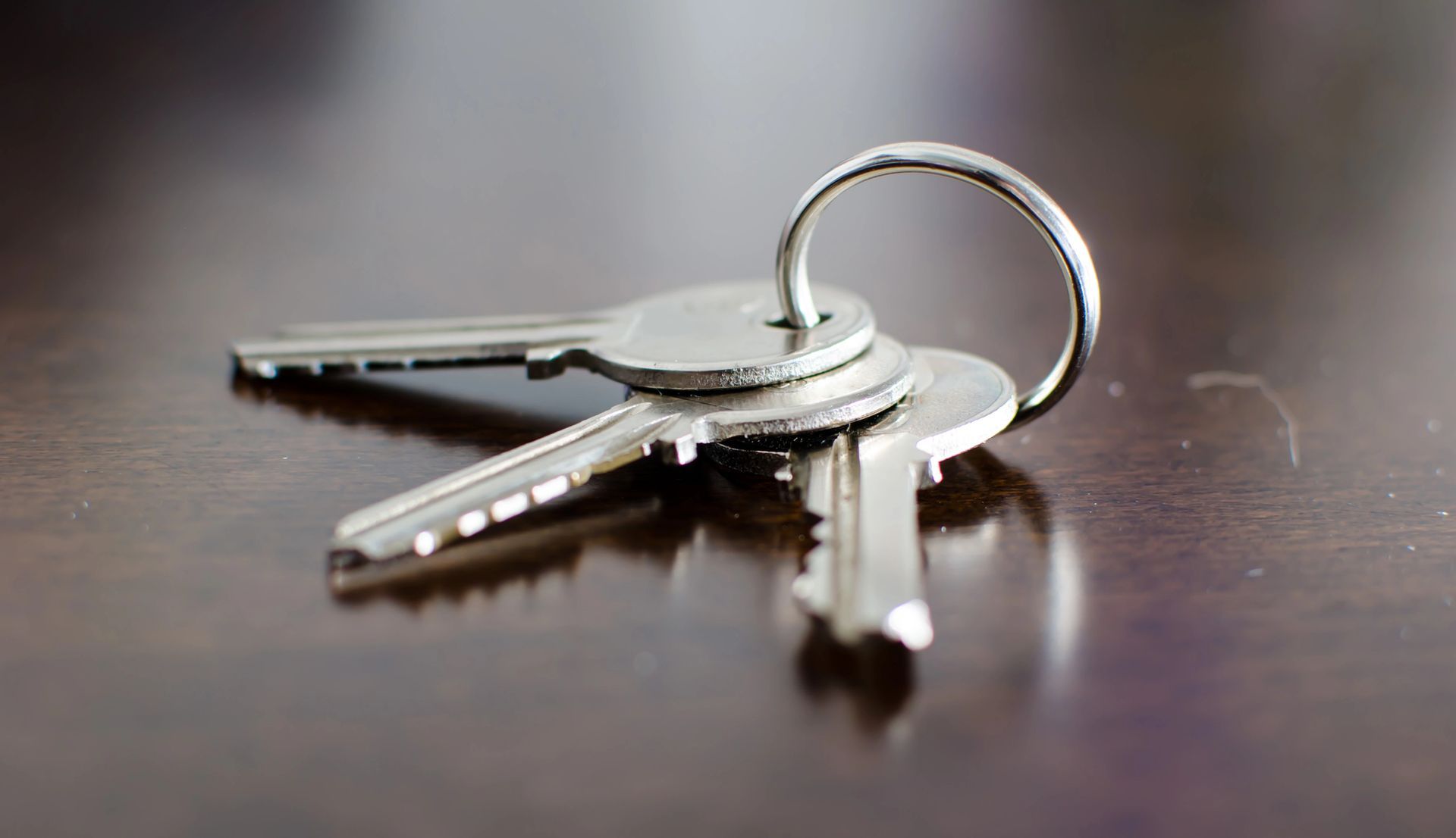 Tre chiavi d'argento su un portachiavi, appoggiate su una superficie di legno riflettente.