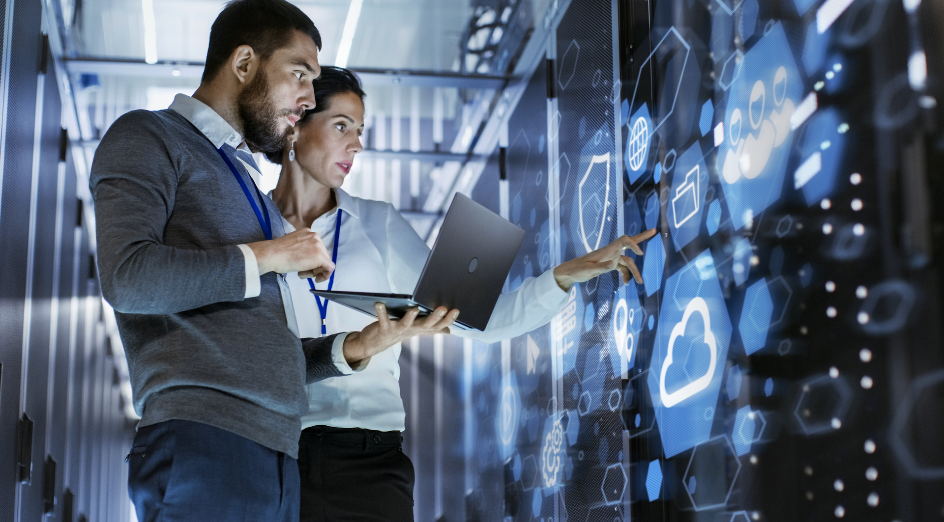 A man and a woman are looking at a laptop in a server room.