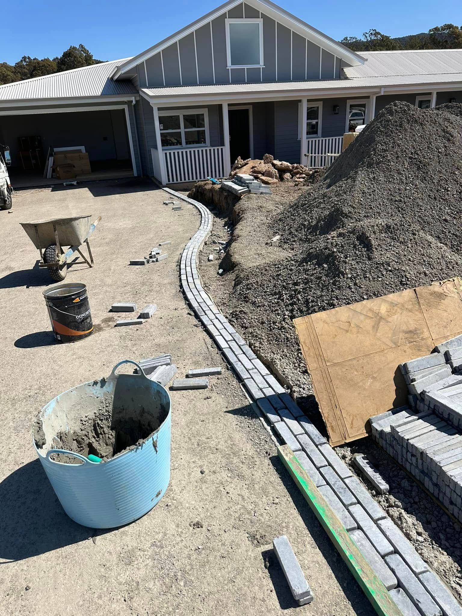 A bucket of cement is sitting on the ground in front of a house under construction.
