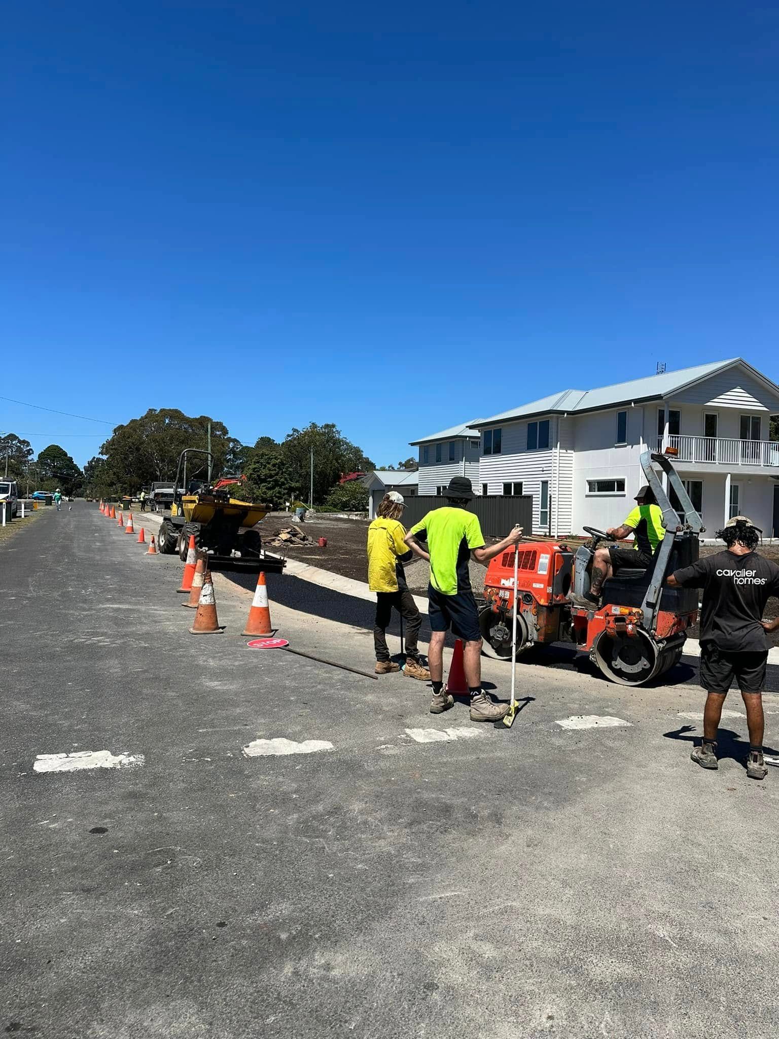 A man is working on a road with a roller and a rake.
