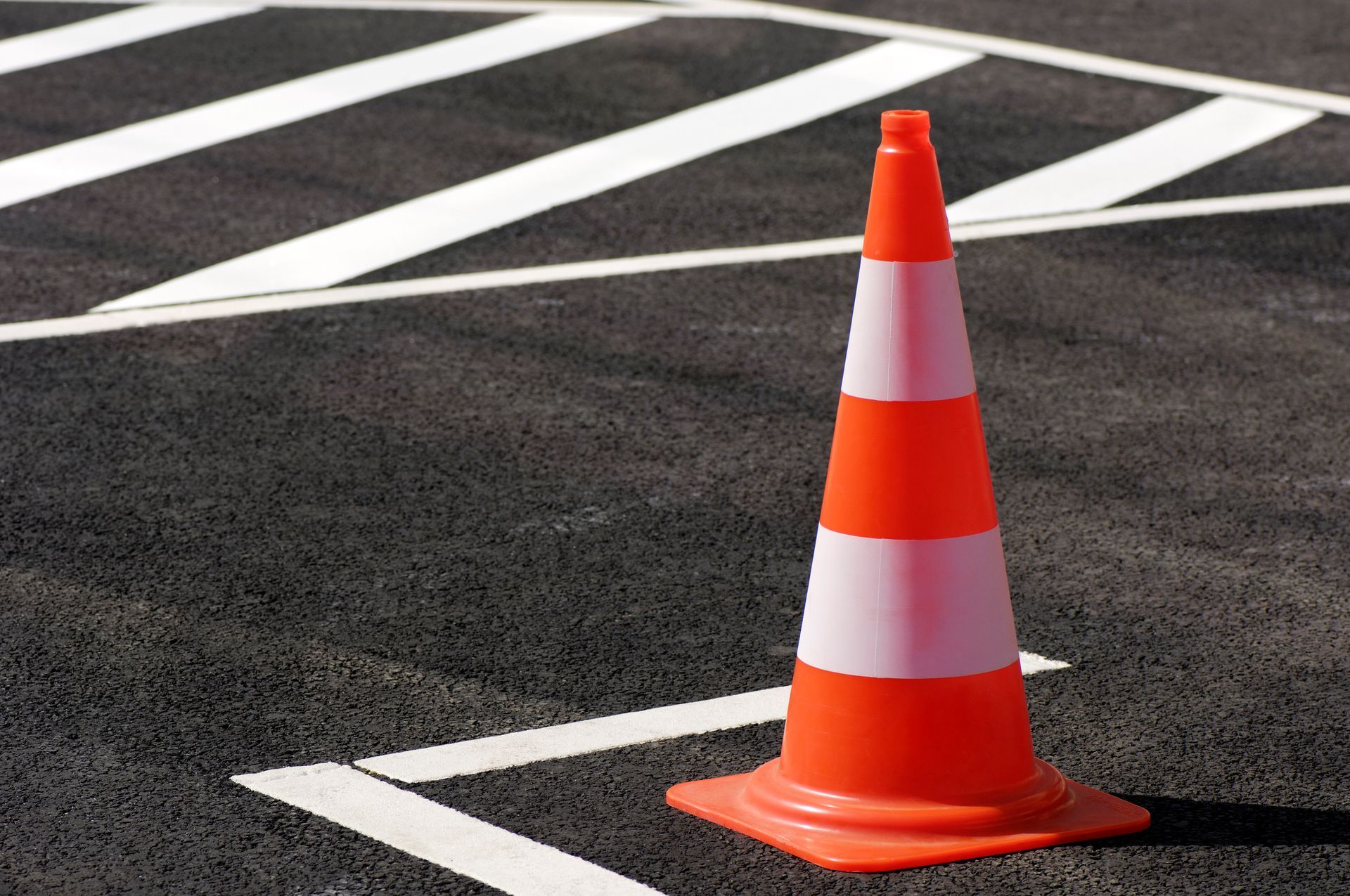 An orange and white traffic cone is sitting on the side of the road.