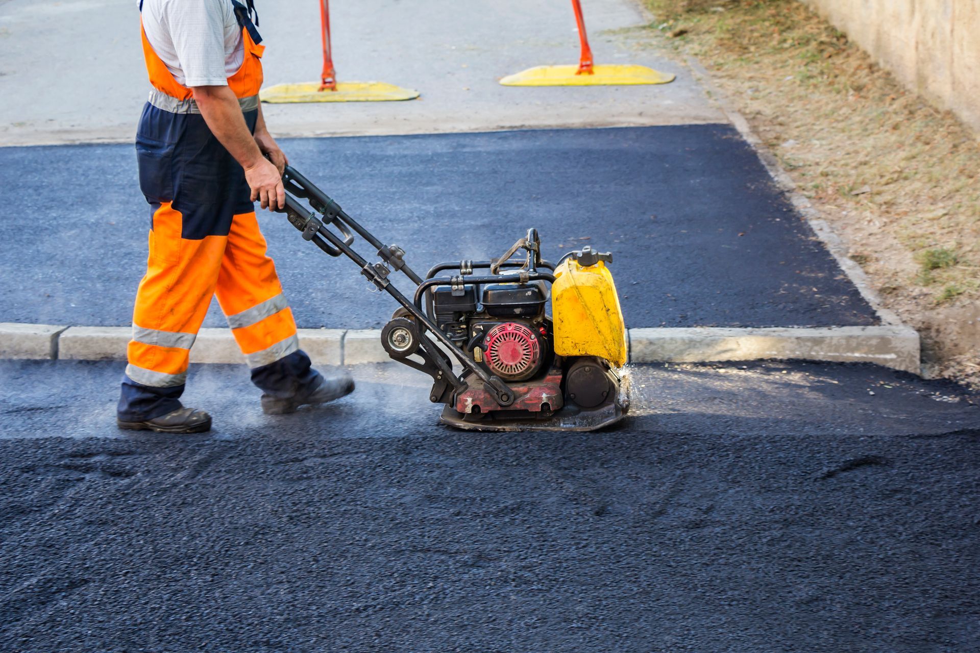 A man is using a machine to compact asphalt on a road.