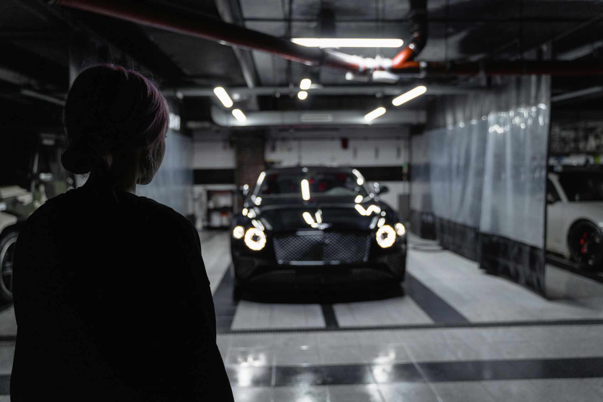 A woman is standing in front of a car in a parking garage.