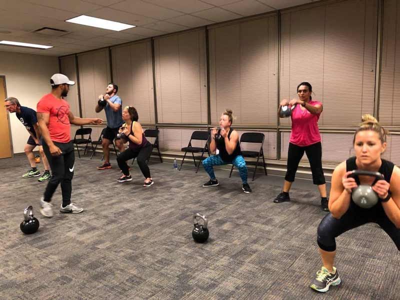 A group of people are doing squats with kettlebells in a gym.