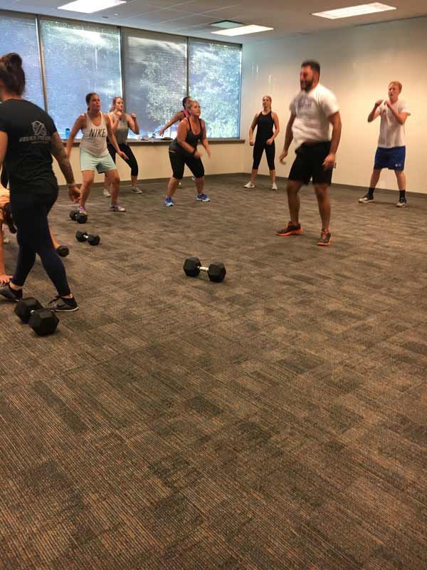 A group of people are dancing in a room with dumbbells on the floor.