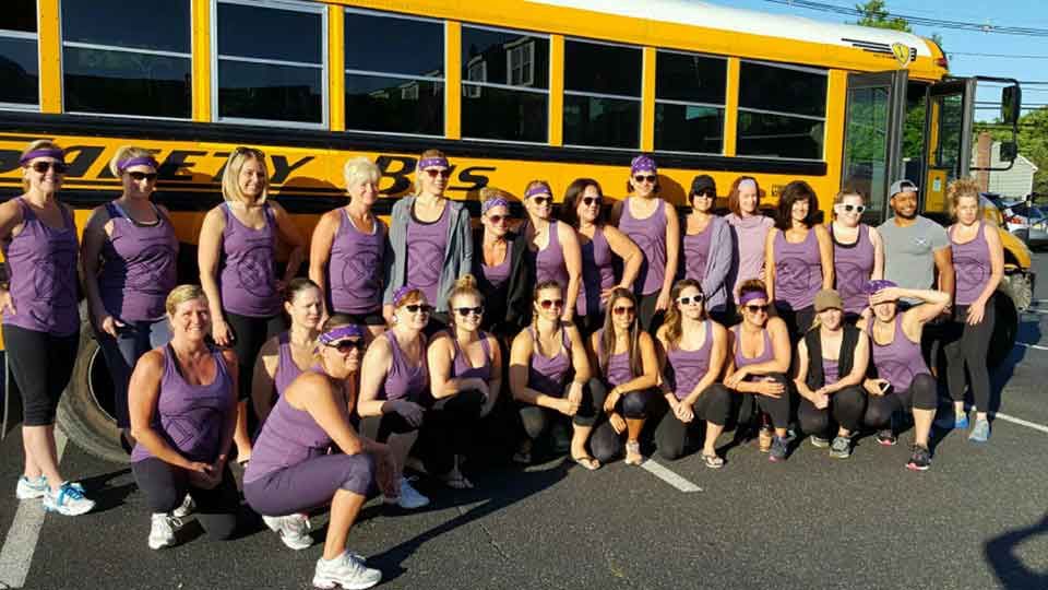 A group of women posing in front of a yellow school bus