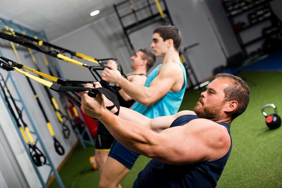 A group of men are doing trx exercises in a gym.