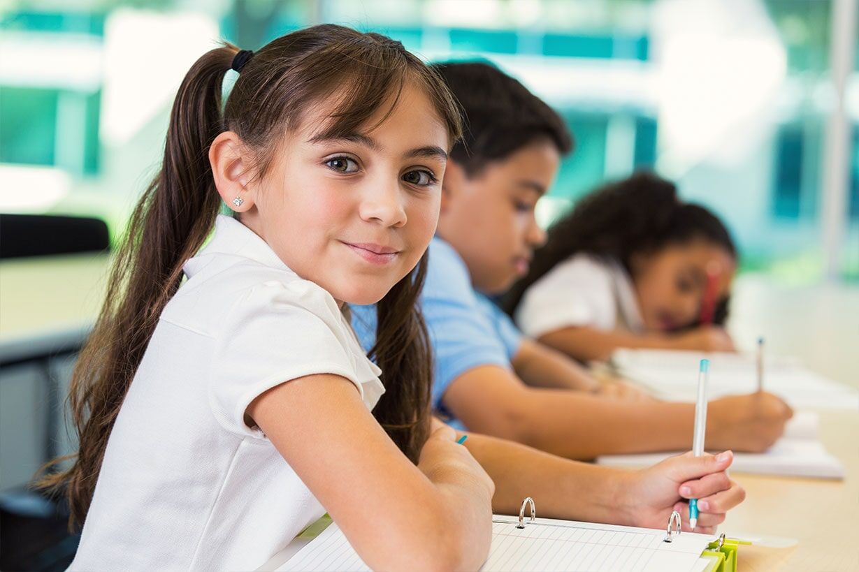 Una niña está sentada en un escritorio en un salón de clases con otros niños.